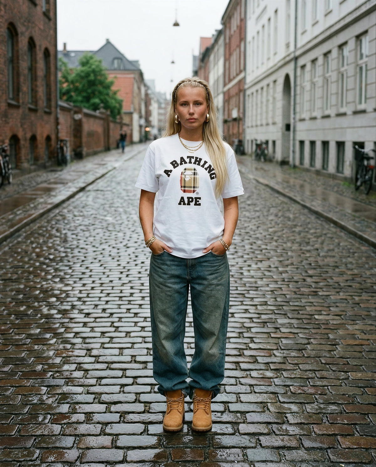 Nainen yllään valkoinen BAPE Check College Tee, jossa beige ruutukuvioinen logo, mukavasti mukulakivikadulla Aarhusissa.